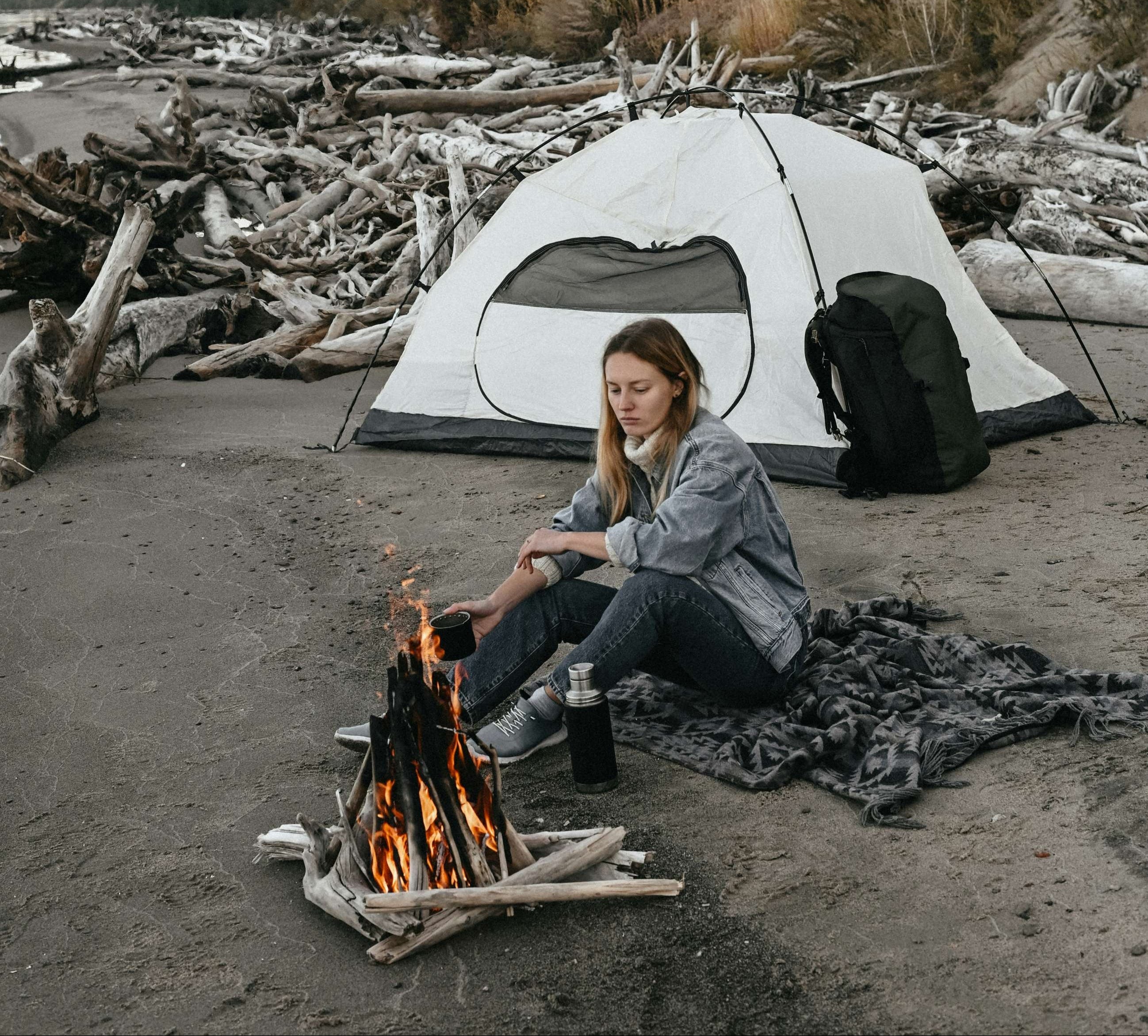 Woman camping on a beach with a tent and fire pit.